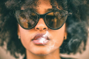 woman wearing sunglasses with smoke coming out her mouth wonders about the effects of synthetic marijuana