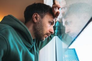 man wearing a green hoodie leans on window and looks out thinking about his issues with cocaine use