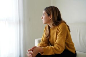 woman sits on a couch looking off into the distance wondering what is self-medicating