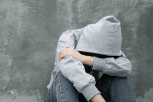 a sitting person in a hoodie rests their head on their arms while struggling with opioid withdrawal symptoms