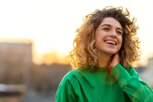 curly haired person smiles and holds their hand to their neck thinking about their recovery goals