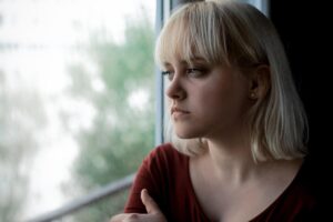 blond woman stands near a window and looks out while thinking about the signs of a fentanyl overdose