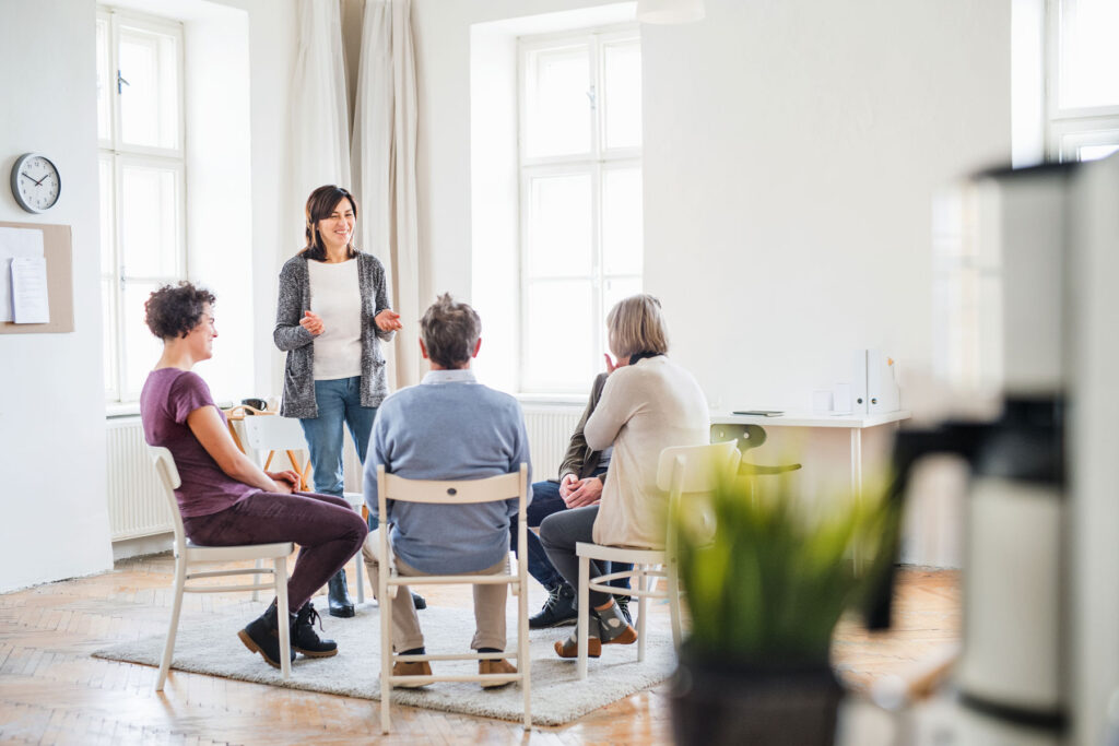 friends in recovery sit in a room together in a circle and talk