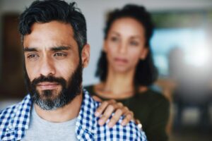 a woman puts her hand on a man's shoulder while discussing with the man about alcoholism effects on family