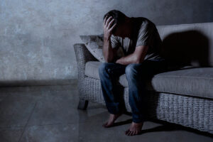 a person sits on a couch in the dark and leans over hold his hand to his head struggling with signs of heroin overdose