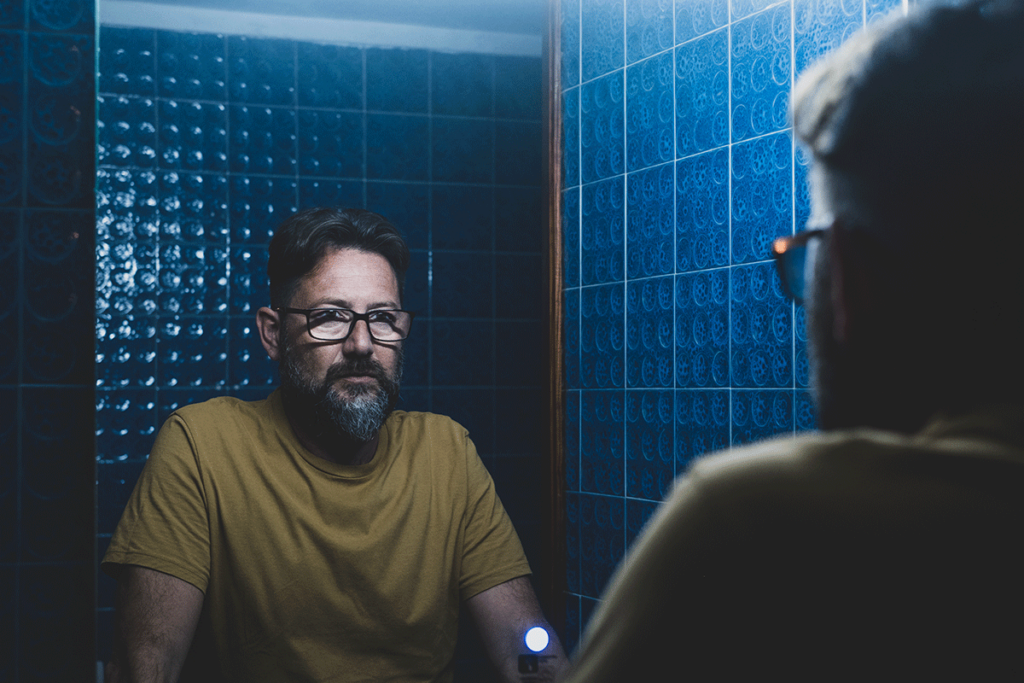 man with glasses looks at his reflection in a mirror and wonders how to get help for alcohol blackouts