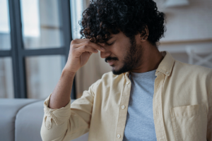 an upset man sits by a window holding the bridge of his nose thinking about the dangers of fentanyl