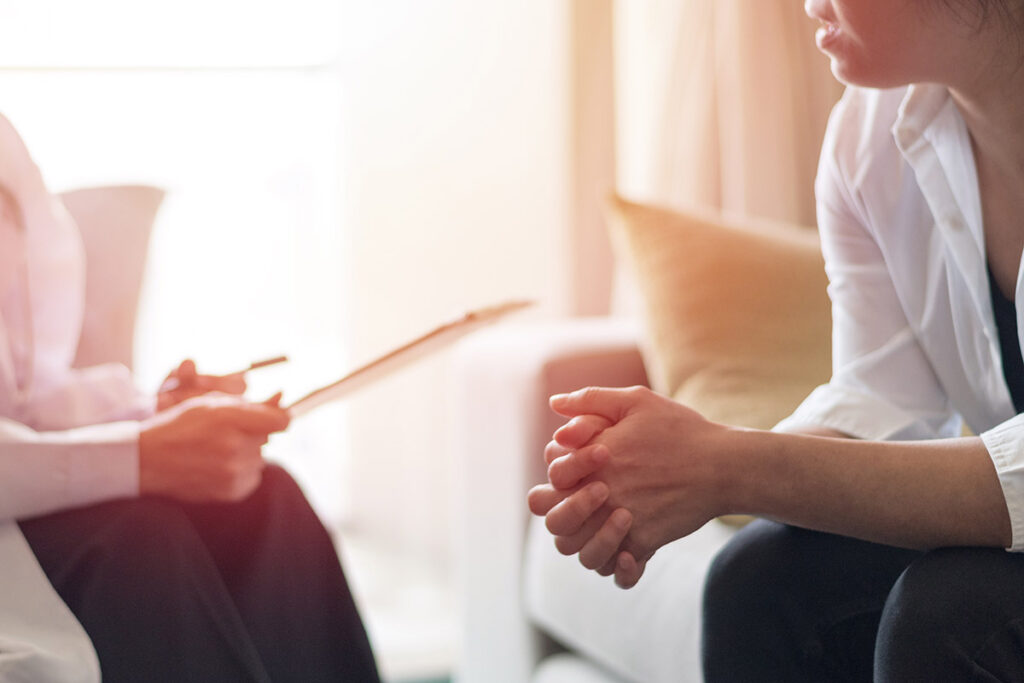 a person leans over with their hands together while listening to their therapist discuss cognitive-behavioral therapy exercises