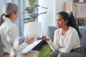 a woman sits on a couch while talking to her therapist and figuring out if cognitive-behavioral therapy is a good option for her