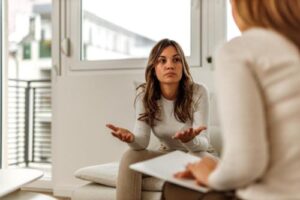 a woman sits on a chair and is talking with her therapist in psychotherapy