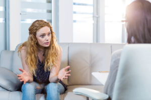 a woman with long hair sits on a couch talking to an addiction specialist about vivitrol treatment