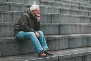 an older adult sits on steps outside and his his hand to his face thinking about what to do after relapse