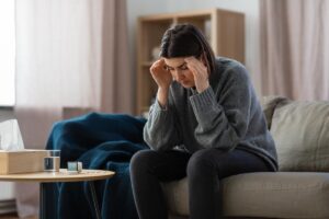 a distressed woman sits on her couch and holds both hands to her temples asking herself is alcohol a stimulant or depressant