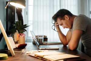 an upset man sits at his desk holding his glasses in his hand and his hand to his forehead while struggling with the realization of long term effects of adderall