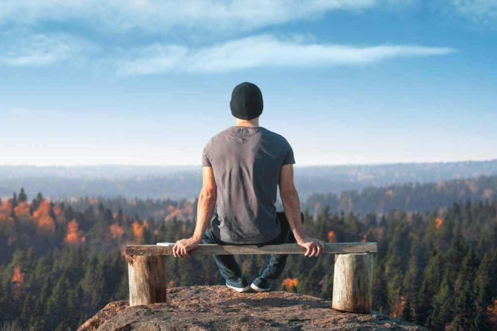 man sits on a bench overlooking a valley and wonders how to stay sober