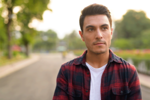 young man in flannel shirt walking along tree-lined street in the afternoon considering 5 facts about addiction