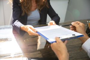 two people sit at desk one person hands paperwork to other that explains the cost of rehab