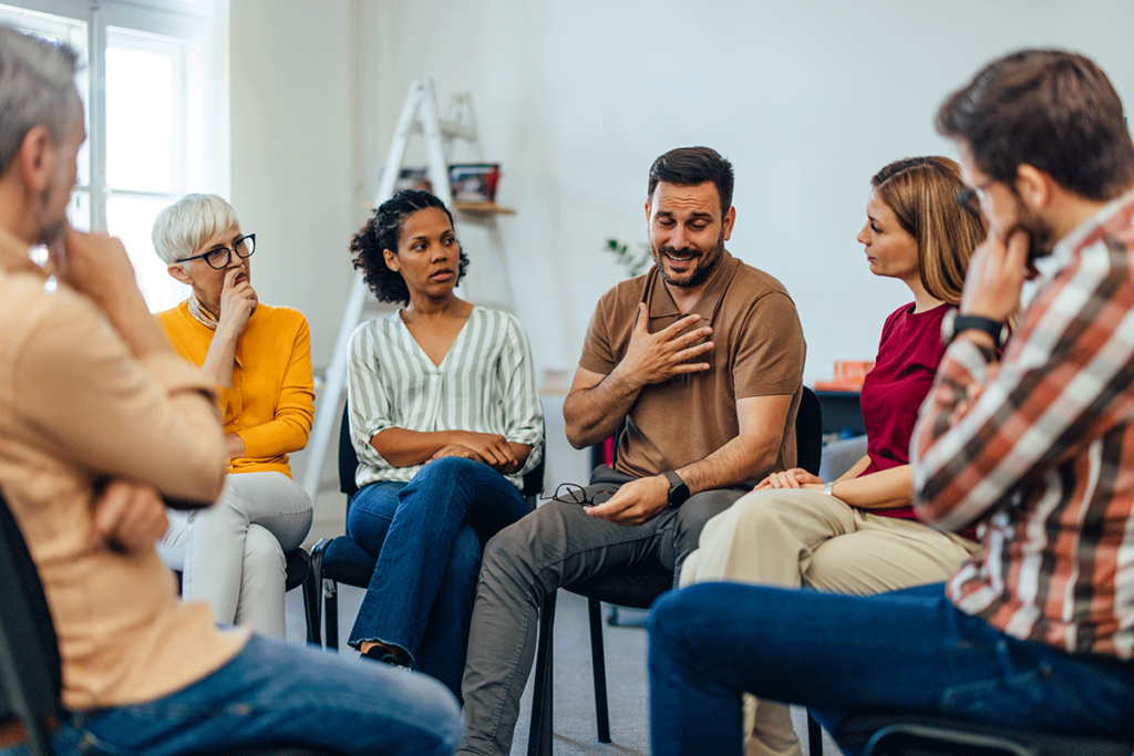 men and women of various ages seated in a circle and engaged in group therapy activities for addiction recovery