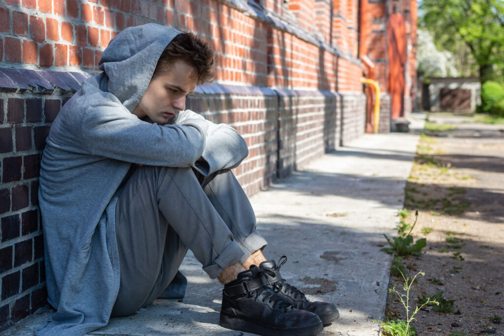 a person in a hoodie sits outside on the ground and thinks about how long does meth stay in your system