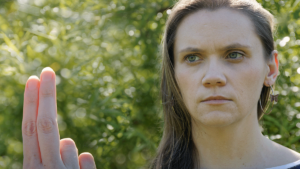 Young woman outside in a wooded area staring intently at her outstretched fingers wondering is EMDR covered by insurance.