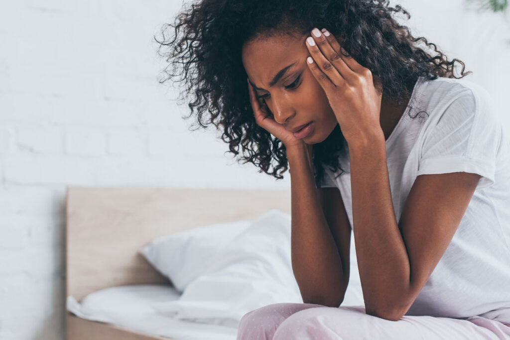 woman sits on her bed holding her hands to her head and experiencing symptoms of adderall withdrawal