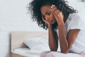 woman sits on her bed holding her hands to her head and experiencing symptoms of adderall withdrawal