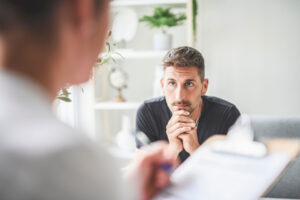 man sits intently listening to therapist talk about healing from childhood trauma and writing notes on their clipboard