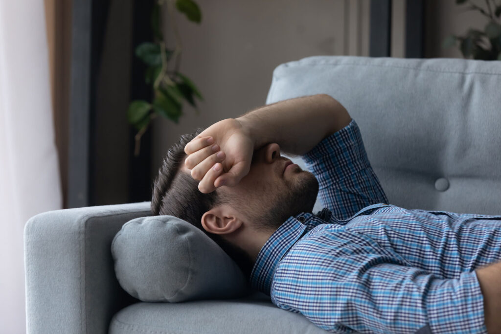 upset man lays on couch with his arm covering his face while wondering how addictive is xanax